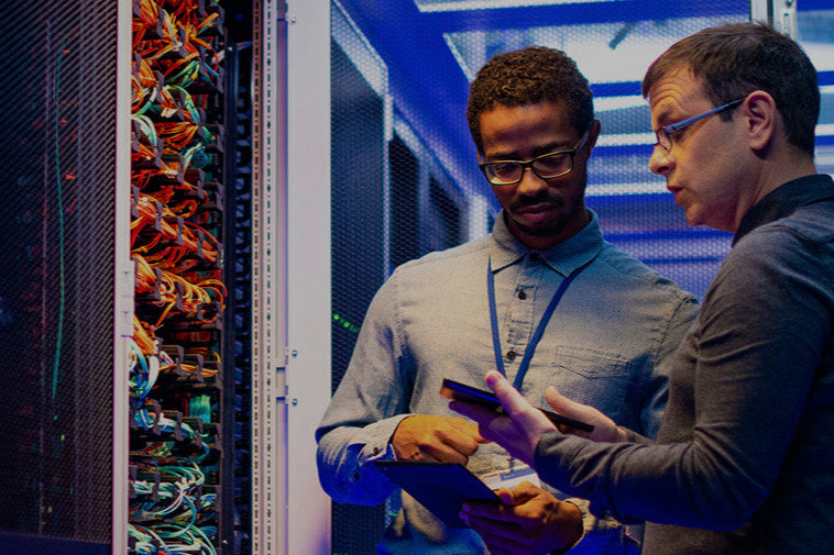 Two technicians working in a server room with equipment and cables visible.
